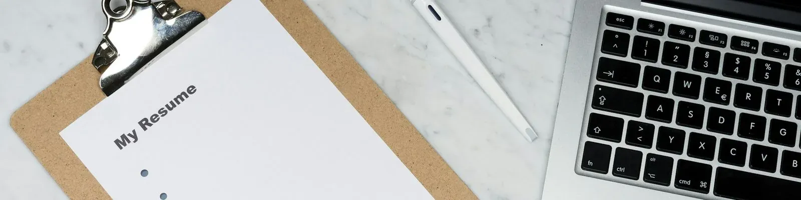 A resume on a clipboard next to a laptop